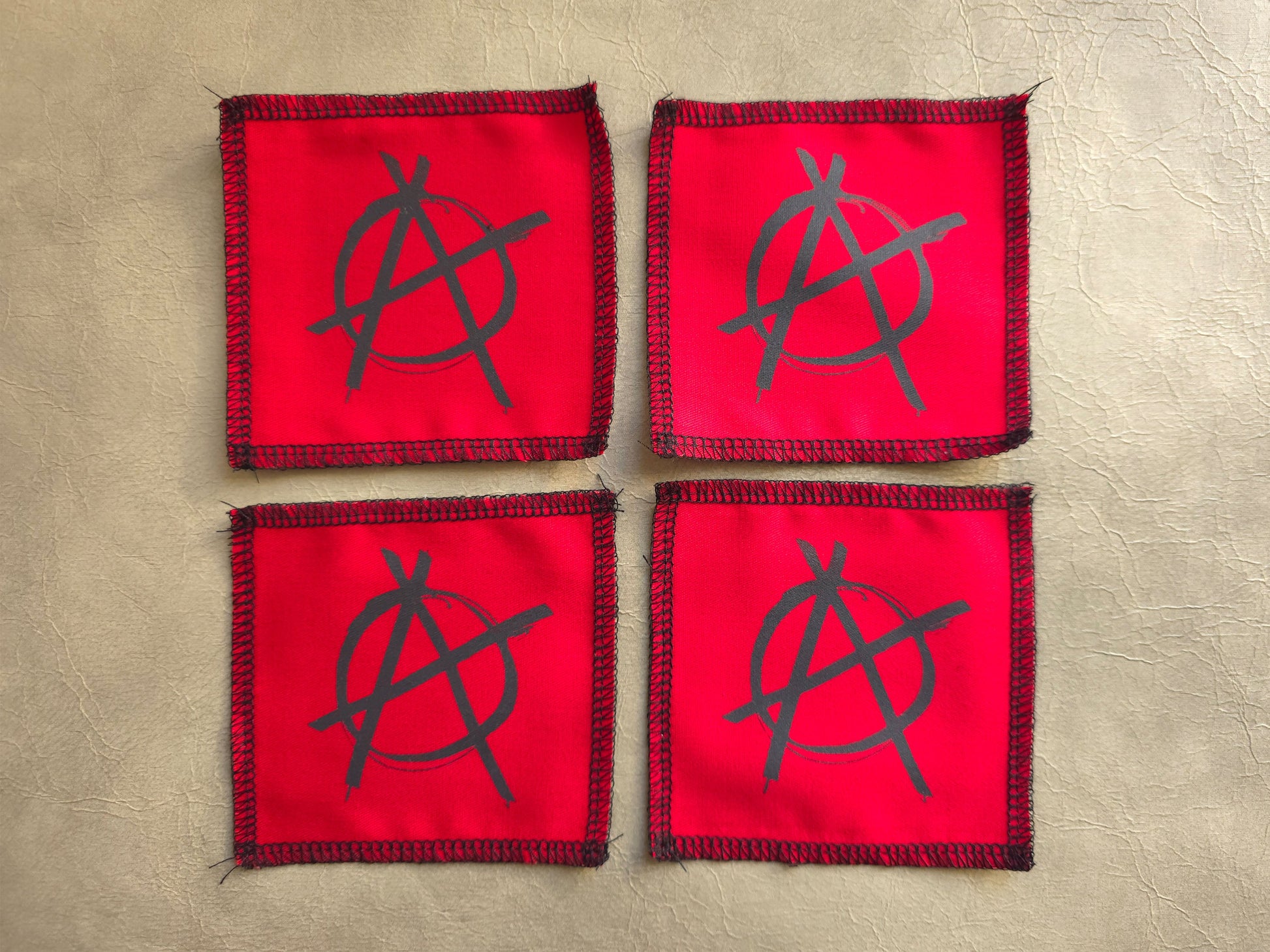 Red handmade screen printed anarchy symbol patches arranged as a collection