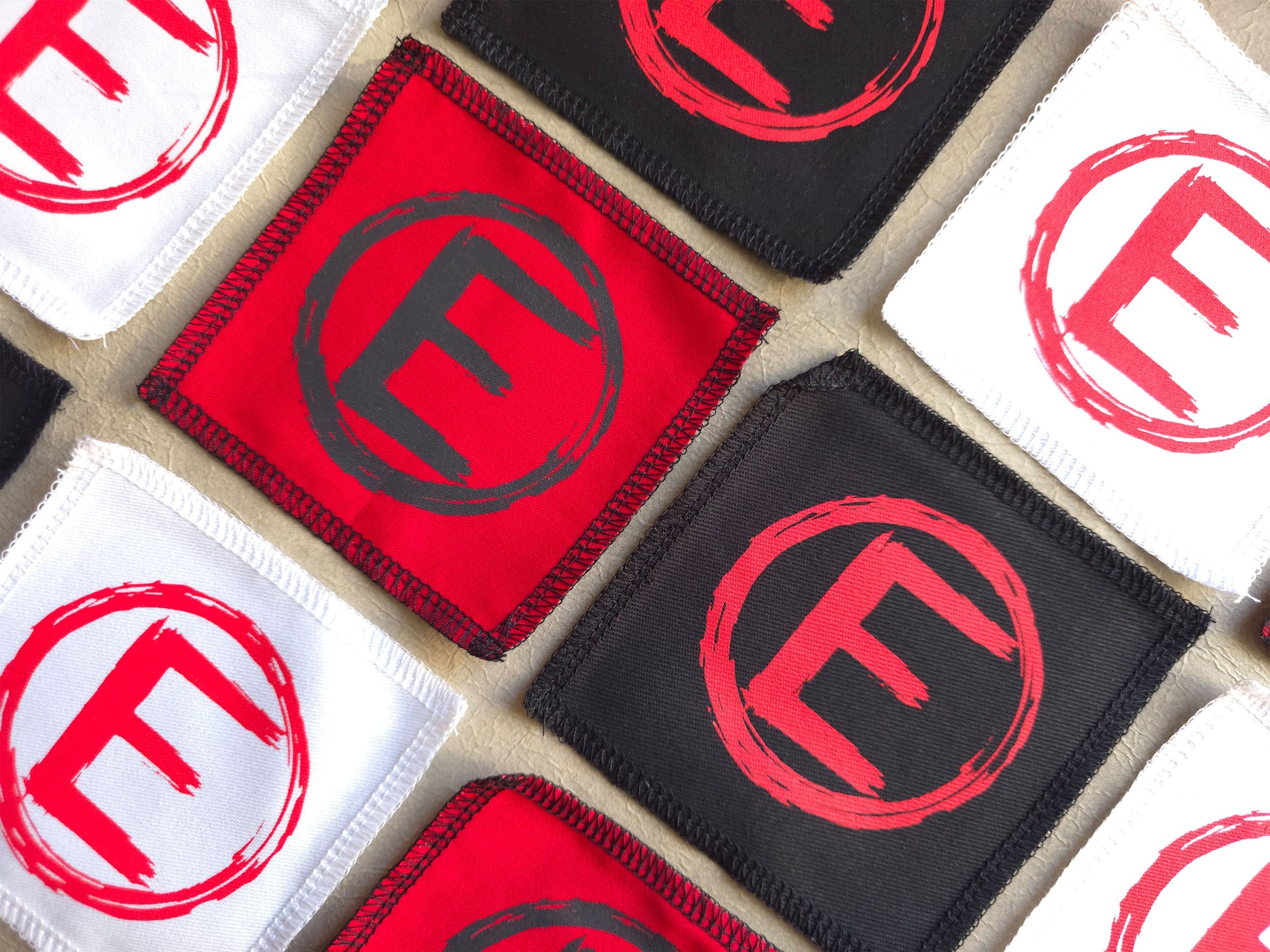 Collection of patches with a red and black 'E' logo on a grid pattern. handmade screen printed patches