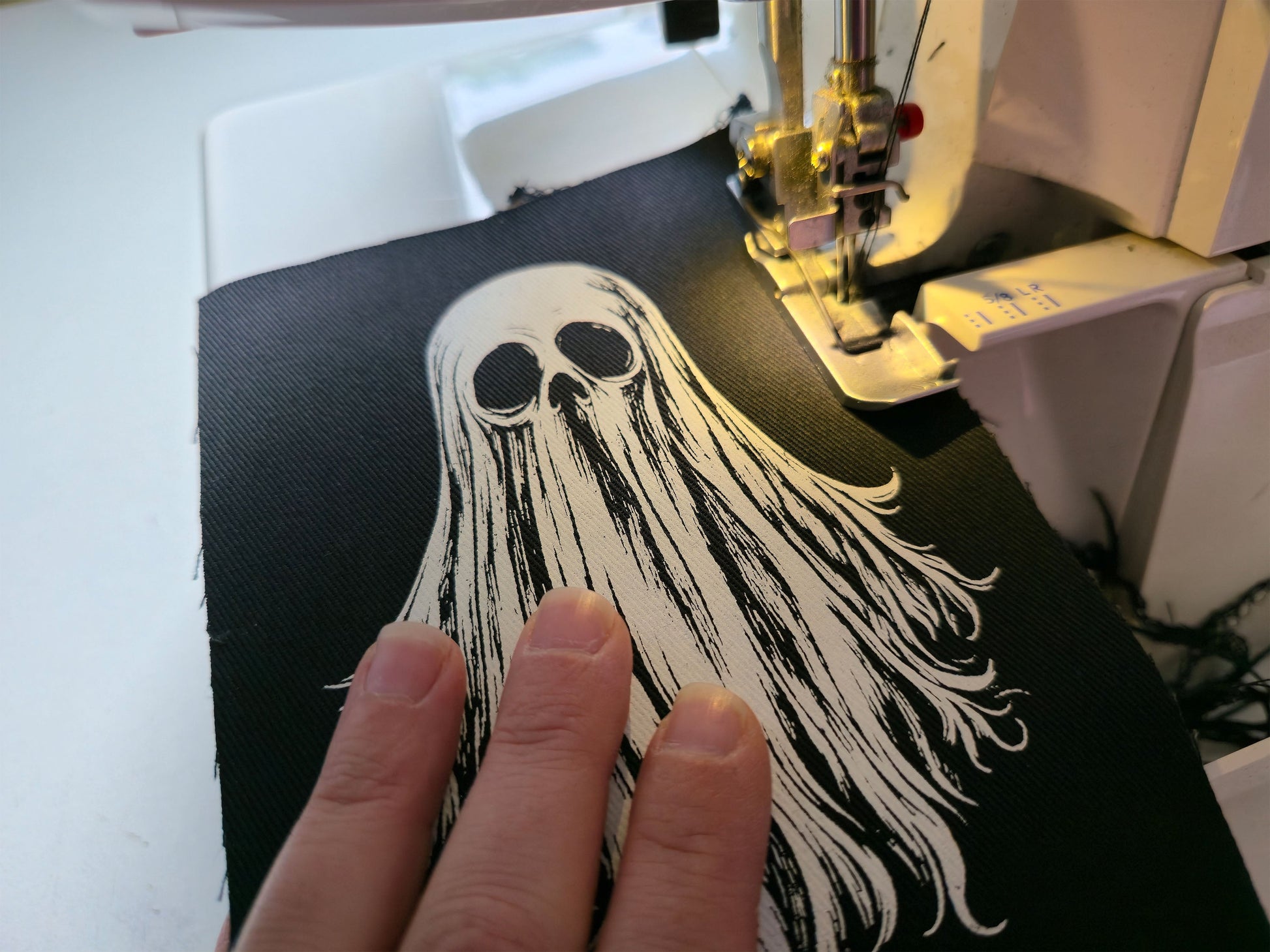 Close-up of sewing machine stitching a handmade ghost patch with needle and thread during the finishing process