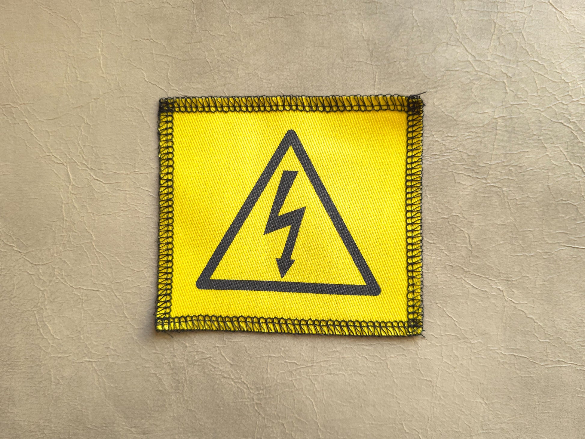 Yellow warning patch with black lightning bolt symbol on a beige background