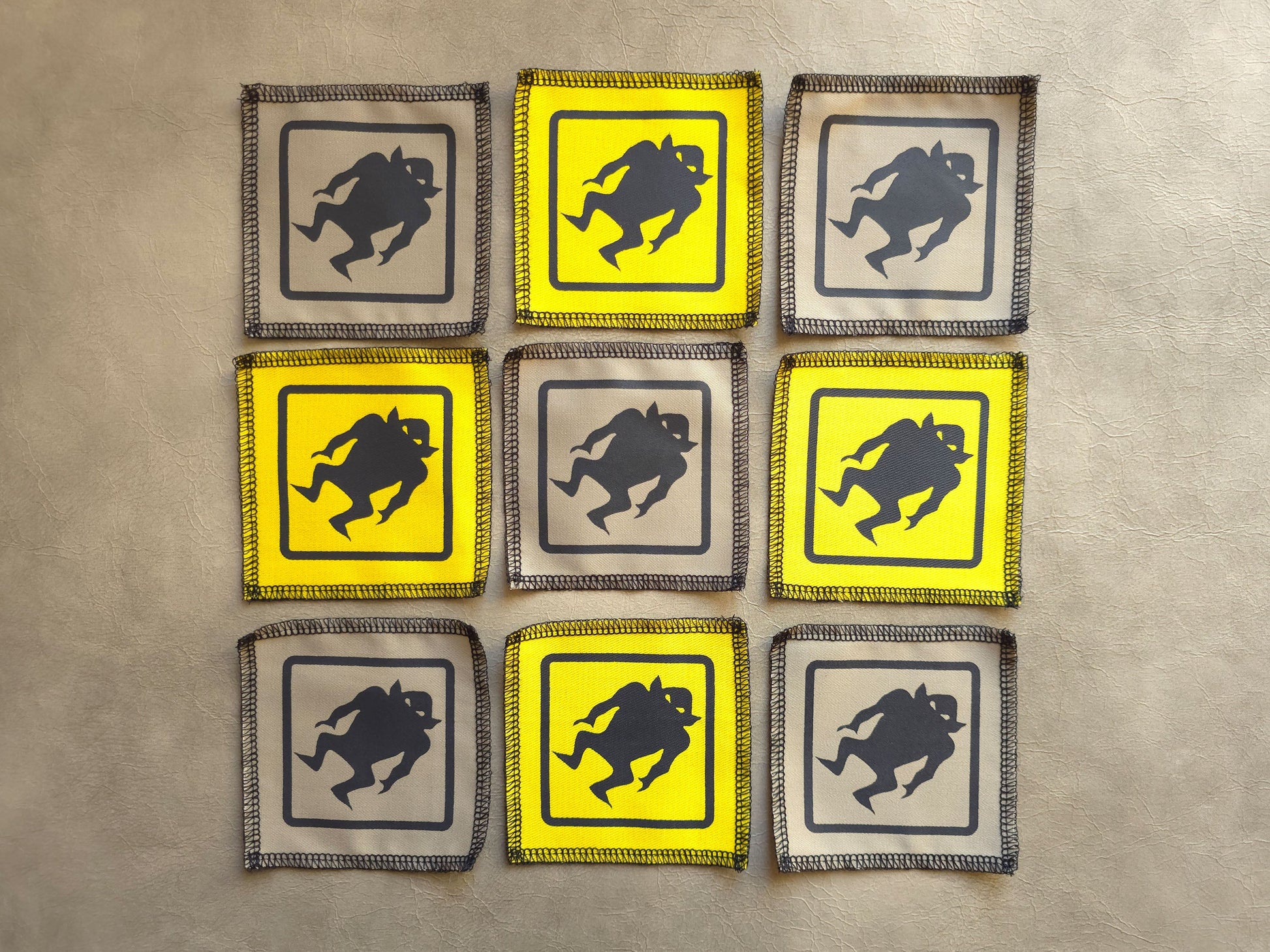 Assorted handmade screen printed monster symbol patches displayed together in yellow and beige colors