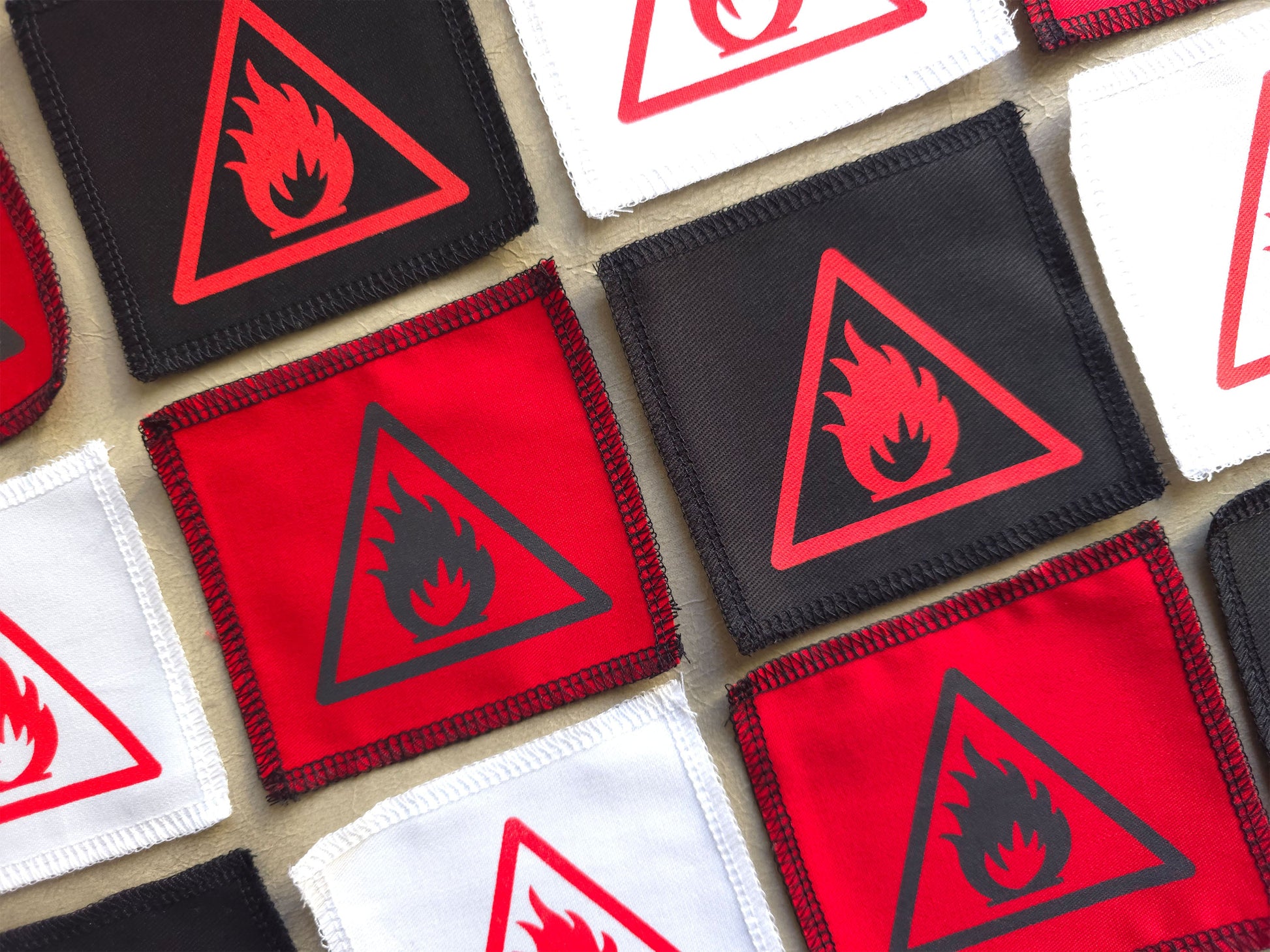 Collection of fabric patches with fire warning symbols on a textured surface
Angled view of handmade screen printed open flame symbol patch highlighting fabric texture and print detail