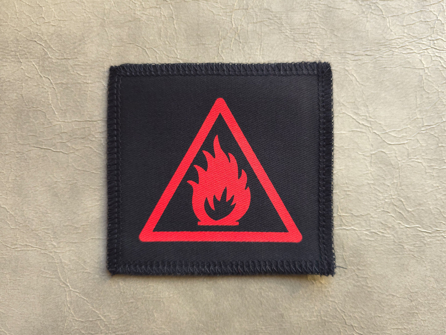 Black patch with red fire symbol on a textured beige background, handmade screen printed patch