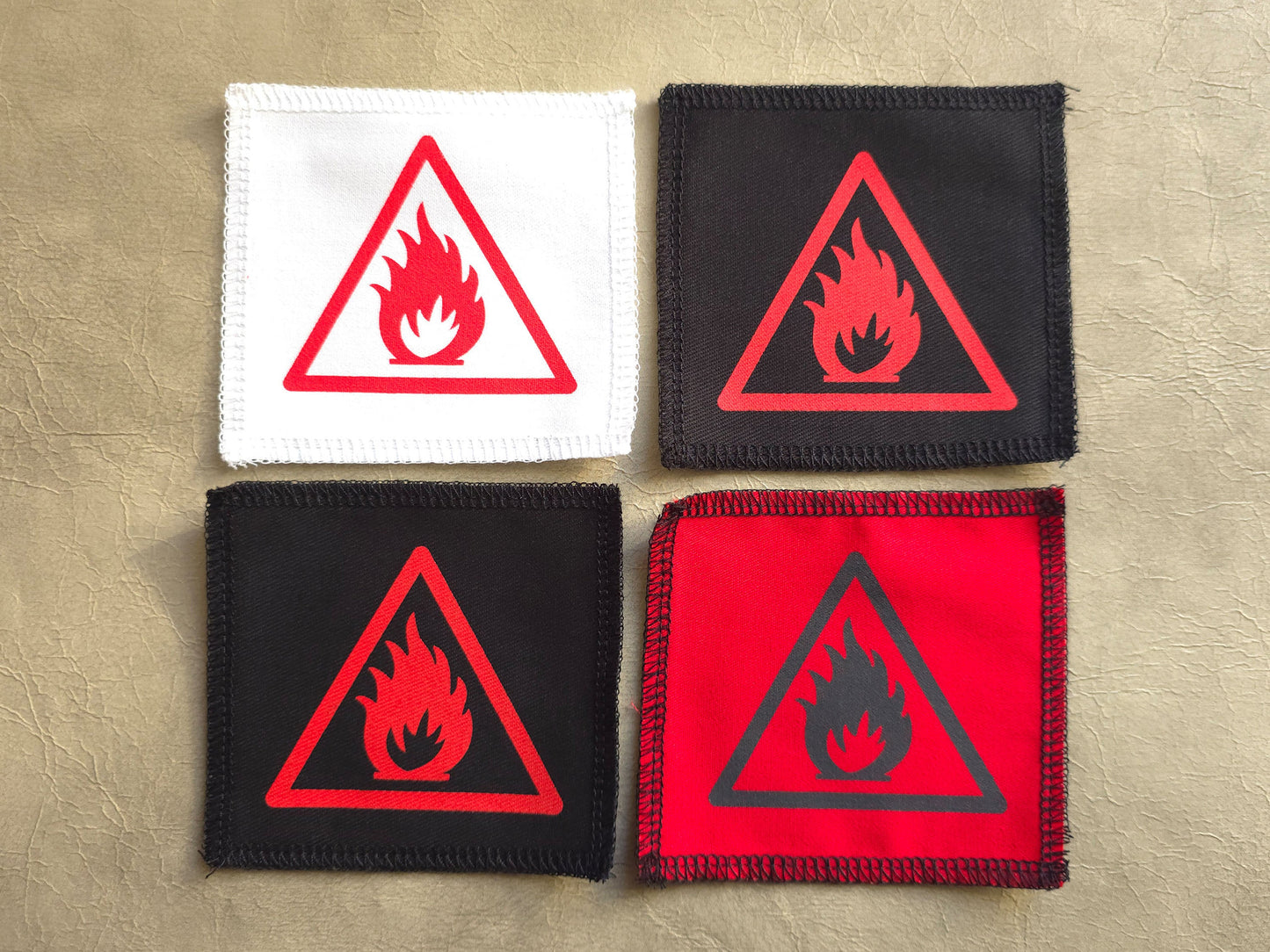 Four fire hazard warning patches in different colors on a beige background