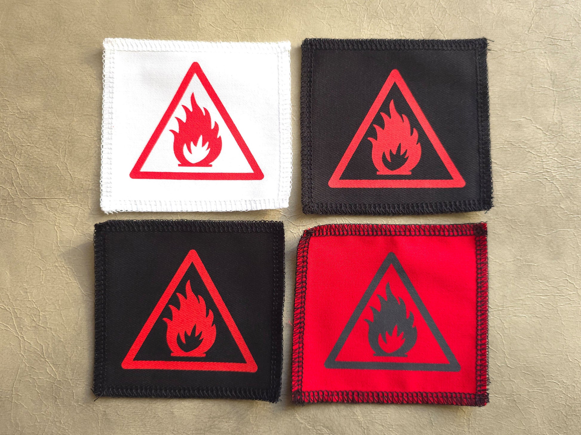 Four fire hazard warning patches in different colors on a beige background