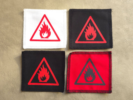 Four fire hazard warning patches in different colors on a beige background