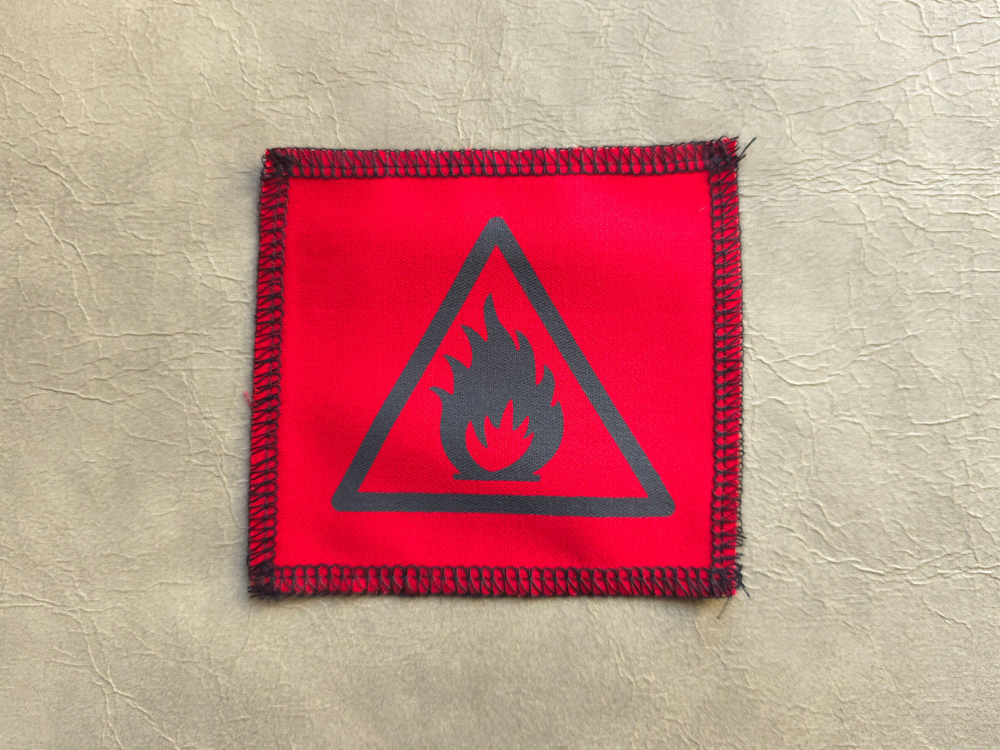 Red fabric patch with a black fire warning symbol on a beige background