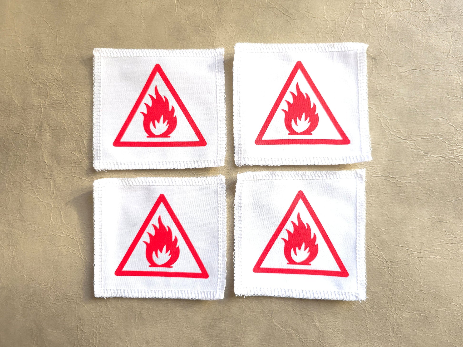 Four white patches with red fire triangle warning symbols on a beige background