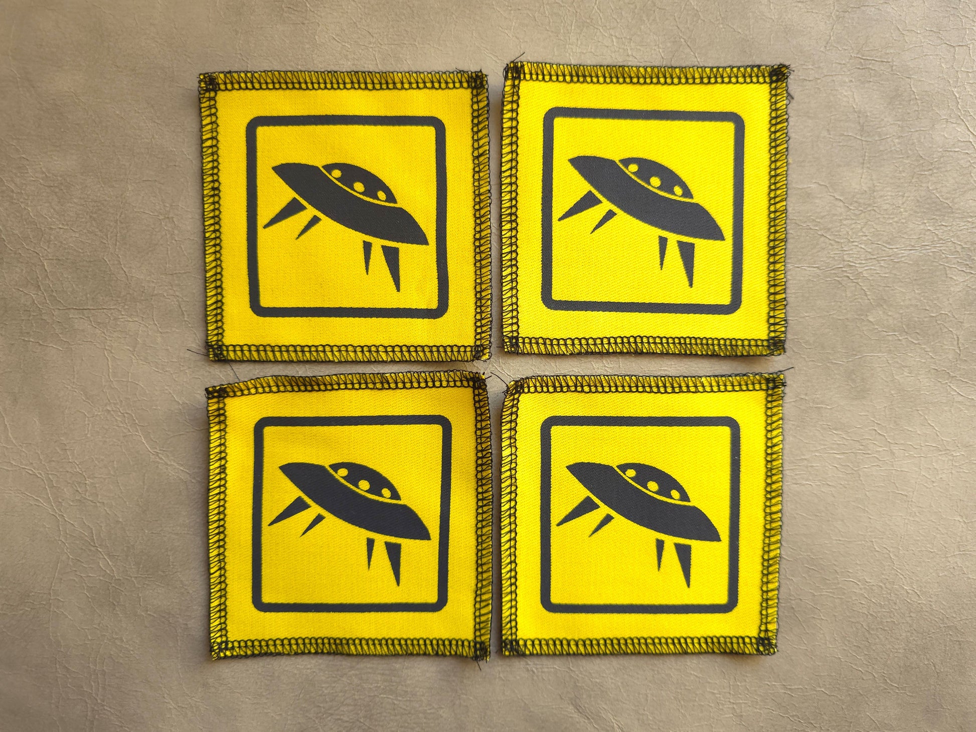 Four yellow patches with black UFO symbols on a beige background