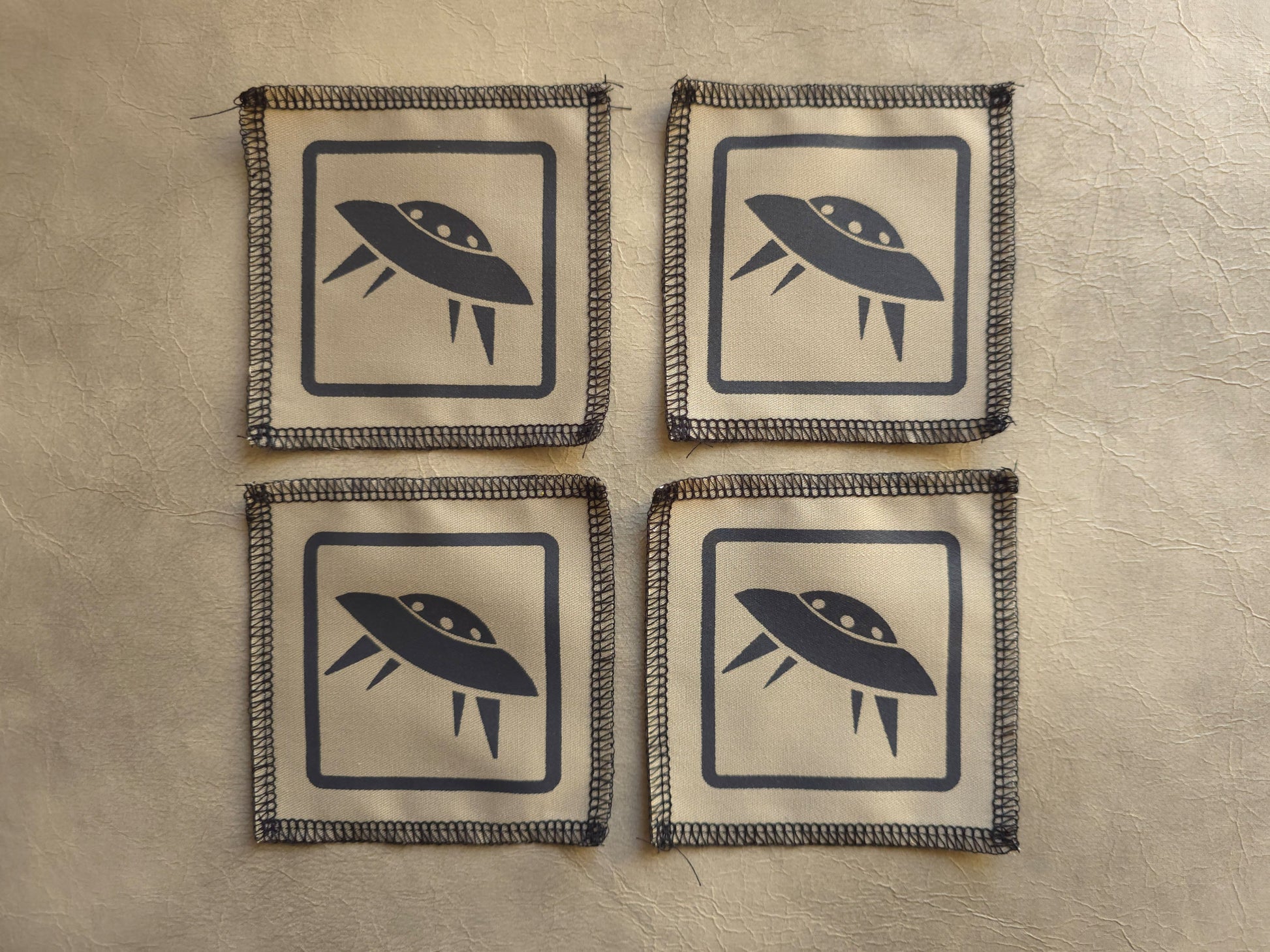 Four square coasters with UFO design on a beige background