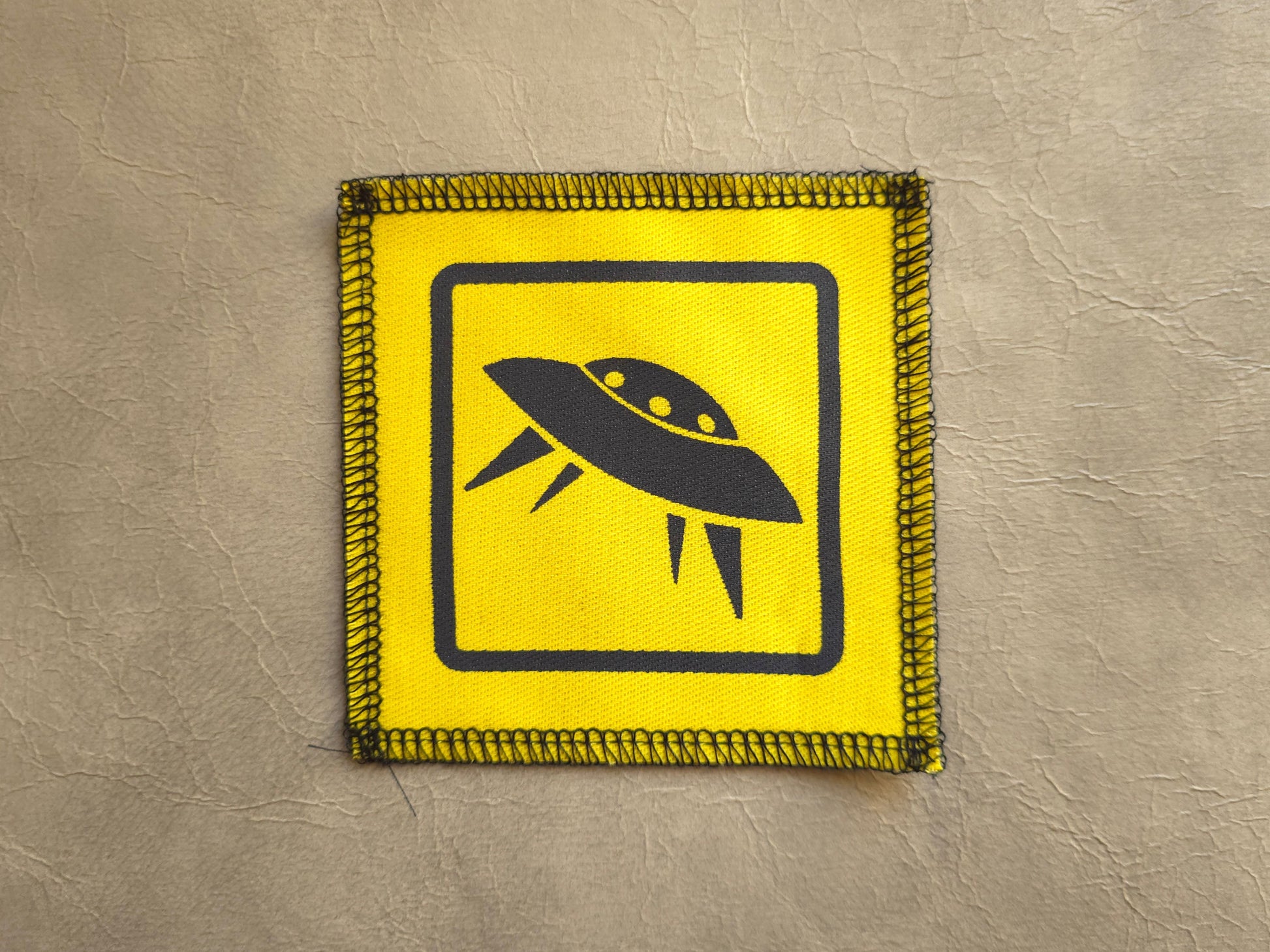 Yellow sign with a black UFO symbol on a textured beige background